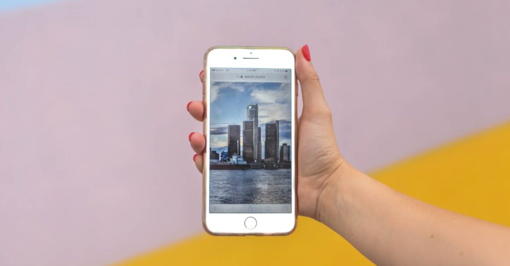 A hand holds a smartphone displaying a Detroit scene against a colorful wall.