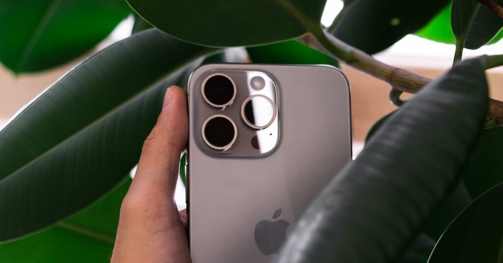 Hand holding a smartphone with triple camera lens against green leaves, showcasing modern design.