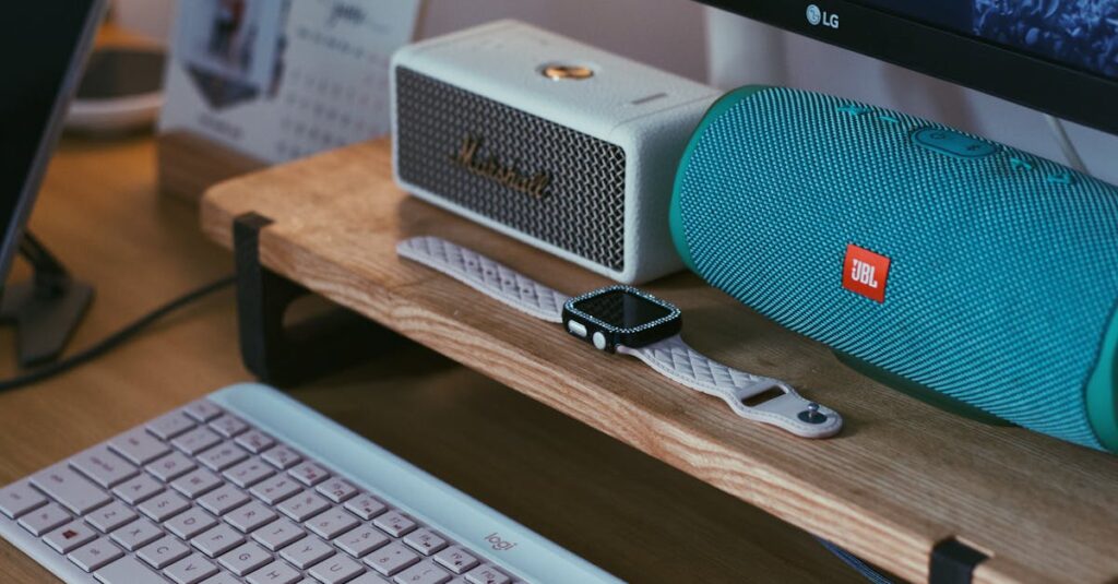 A close-up of a modern workspace featuring Bluetooth speakers, a smartwatch, and a keyboard.