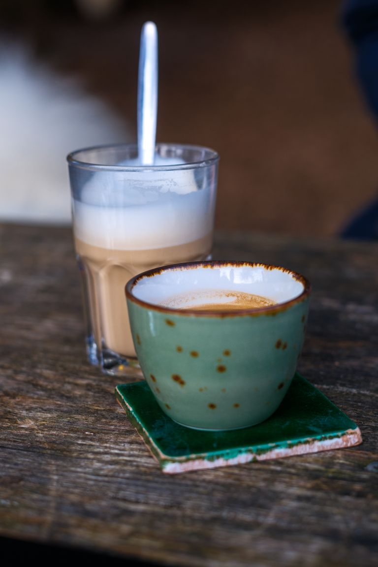 A warm and inviting café setting featuring a glass of latte and a ceramic espresso cup on a wooden table.